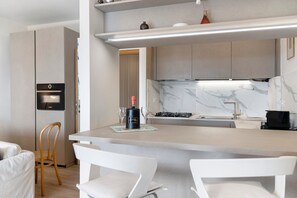 A modern kitchen with a built-in oven, a marble backsplash, and a bar area with two white chairs. - Terrace by the Sea Apartment with Sea View, Terrace, and Scenic Trails (Lavagna)