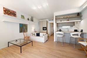 A modern living space with a glass-top table, a white sofa, and a kitchen area with bar stools. - Terrace by the Sea Apartment with Sea View, Terrace, and Scenic Trails (Lavagna)