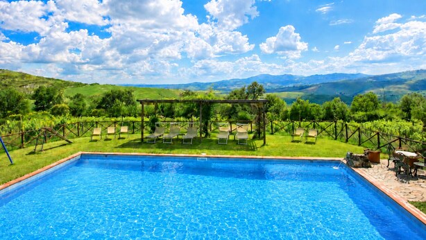 A swimming pool with a pergola and lounge chairs, surrounded by a lush green landscape and distant mountains. - An old Tuscan stone farmhouse with a pool and vineyard in the Val d'Orcia (Radicofani)
