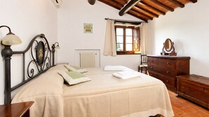 A bedroom with a bed, a dresser, a radiator, a window with curtains, and a picture on the wall. - An old Tuscan stone farmhouse with a pool and vineyard in the Val d'Orcia (Radicofani)