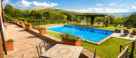 Ein Pool mit Pergola, Liegestühlen und Tisch auf einer Terrasse mit Blick auf Hügel.