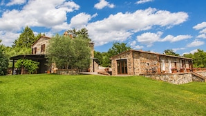 A stone building with a rustic design, a covered patio, and a lush green lawn. - An old Tuscan stone farmhouse with a pool and vineyard in the Val d'Orcia (Radicofani)