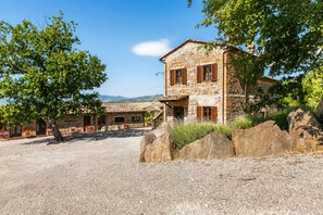 A stone building with a gravel driveway, surrounded by large rocks and trees. - An old Tuscan stone farmhouse with a pool and vineyard in the Val d'Orcia (Radicofani)
