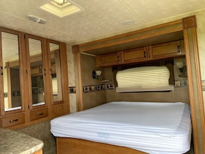 A compact RV interior with a bed, wooden cabinets, and a small kitchenette.