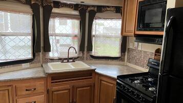 A compact RV kitchen with a sink, stove, and microwave.