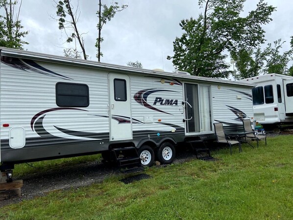 A PUMA RV with a sliding door, a small attached utility vehicle, and a bench outside.
