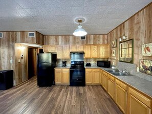 Une cuisine avec des meubles de rangement en bois, un réfrigérateur noir, une cuisinière et un four à micro-ondes.