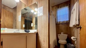 Une salle de bain avec un meuble-lavabo en bois, des toilettes et une poubelle.