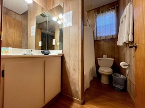 Une salle de bain avec un meuble-lavabo en bois, des toilettes et une poubelle.