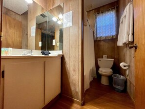 Une salle de bain avec un meuble-lavabo en bois, des toilettes et une poubelle.