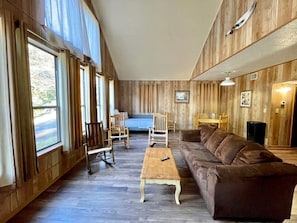 Un salon spacieux doté d’une grande fenêtre, de murs en bois, d’un canapé marron, d’une table basse en bois et d’un coin repas avec des chaises et une table.