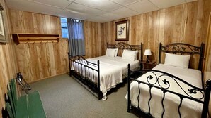 Une chambre avec deux lits, un lambris en bois, une fenêtre avec des rideaux, un tableau encadré au mur et une petite table avec une lampe.