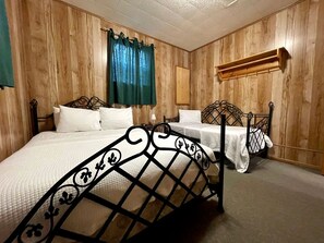 Une chambre avec deux lits, des murs lambrés, un rideau vert, une étagère en bois et un luminaire fixé au mur.