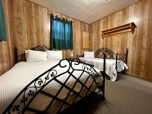 Une chambre avec deux lits, des murs lambrés, un rideau vert, une étagère en bois et un luminaire fixé au mur.