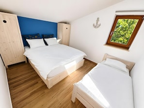 Ein Schlafzimmer mit zwei Betten, einem Kleiderschrank, einem Fenster mit Blick auf Grünflächen und einer Wanddekoration.