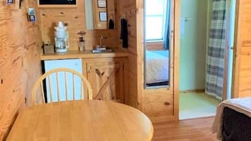 A compact room with a wooden interior, a dining table with chairs, a microwave, a small sink, and a bed.