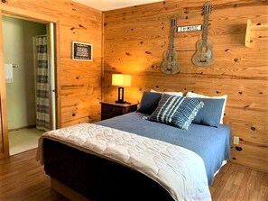 Een kamer met houten lambrisering, een bed, een gitaar en een bordje met de tekst 'I ♥ MUSIC'.