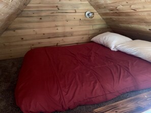 Una habitación con techo de madera inclinado, colcha roja y almohada blanca.