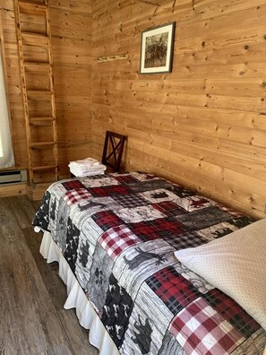 Una habitación de cabaña de madera con una cama, una escalera y un cuadro en la pared.