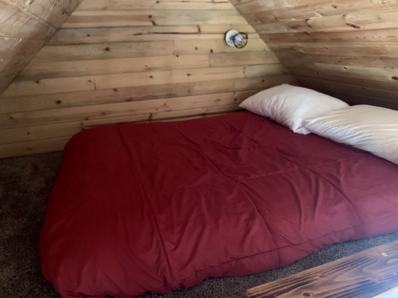 Ein Zimmer mit Holzbalkendecke, einer roten Tagesdecke und einem weißen Kopfkissen.