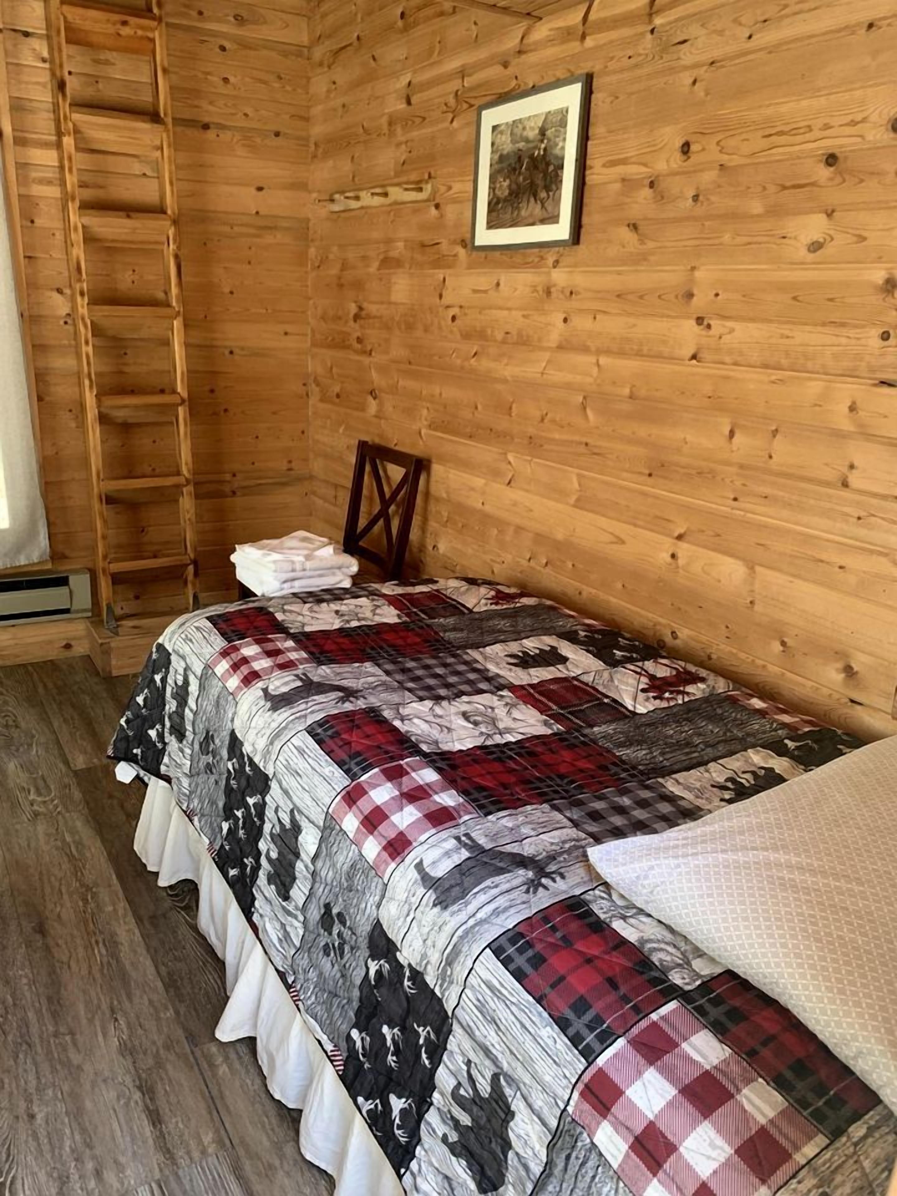 A wooden cabin room with a bed, a ladder, and a framed picture on the wall.