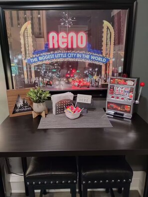 Ein Schreibtisch mit Blick auf eine Stadtkulisse in einem Bilderrahmen, ein Spielautomat, eine Schale mit Snacks und eine kleine Pflanze.