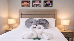 Ein ordentlich gemachtes Bett mit zwei schwanenförmigen Handtüchern, zwei grauen Kissen und drei Reno-Filmplakaten an der Wand.