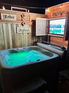 Ein Whirlpool mit rustikaler Holzvertäfelung, einem Schild mit der Aufschrift 'Relax' und einem Fenster mit Blick auf Bäume.