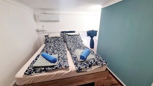 Ein Einzelbett mit gemusterten Betttextilien, ein kleiner Nachttisch und eine wandmontierte Klimaanlage.
