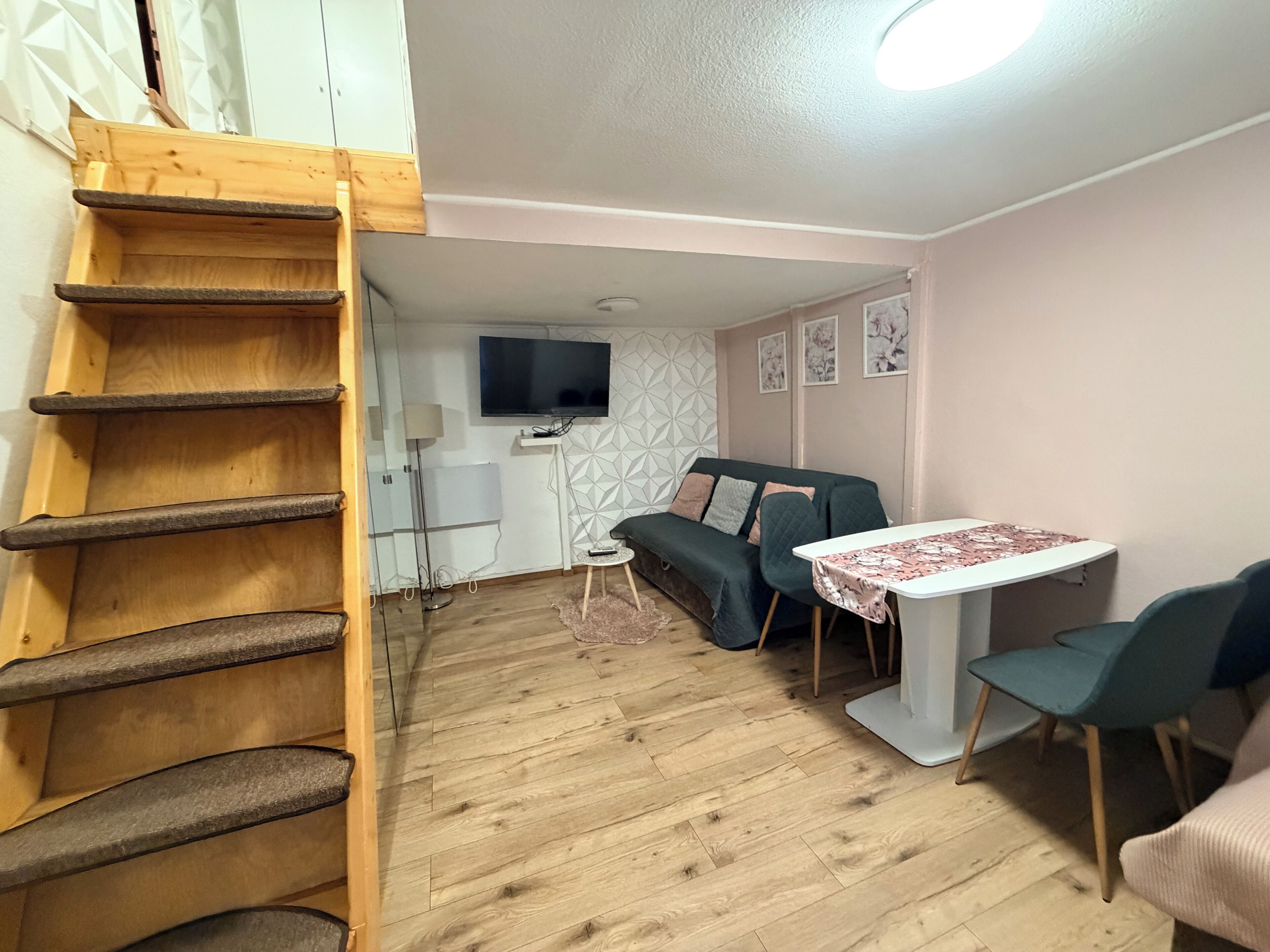 A room with a wooden ladder, a sofa, a table, and a TV mounted on the wall.