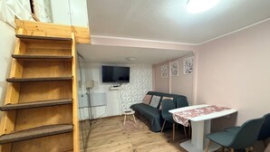 Une pièce avec une échelle en bois, un canapé, une table et un téléviseur fixé au mur.