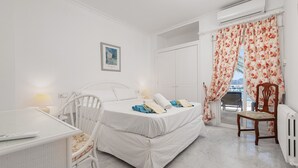 Ein Schlafzimmer mit Bett, Schreibtisch, Stuhl, Heizkörper und einem Fenster mit Vorhängen.