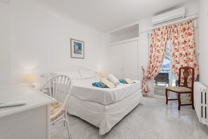 Quarto com cama, escrivaninha, cadeira, radiador e janela com cortinas.