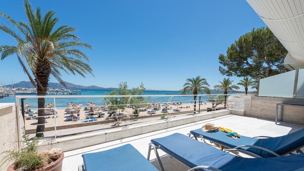 Ein Balkon mit Liegestühlen, Blick auf den Strand und eine Palme.