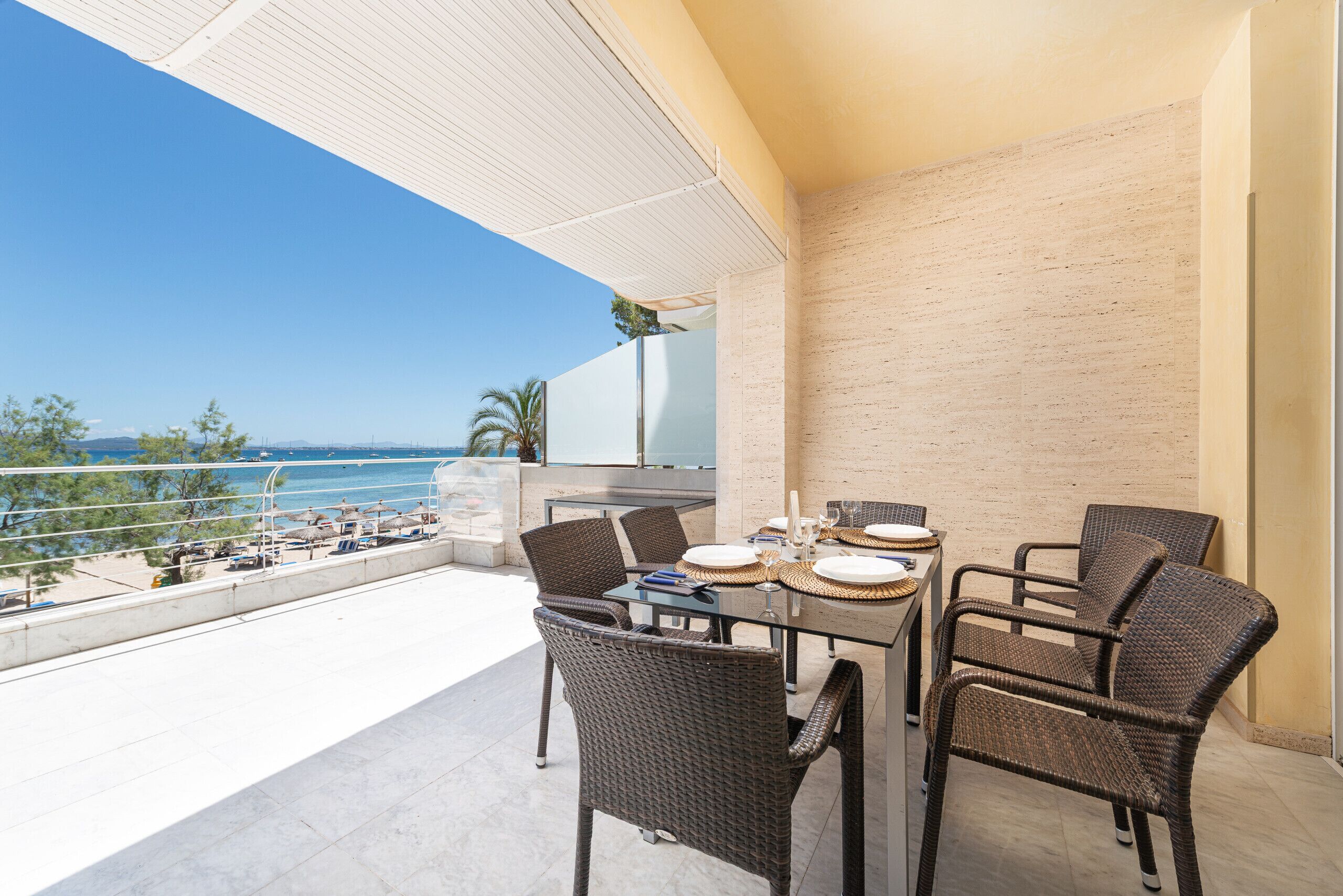 A balcony with a table set for dining, wicker chairs, and a view of the sea.