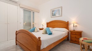 Une chambre à coucher avec un lit en bois, une table de chevet, une commode, une fenêtre avec des stores et un tableau encadré au mur.