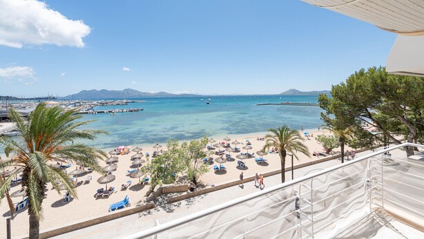 Une plage avec vue sur la mer, des parasols, des palmiers et un ciel dégagé.