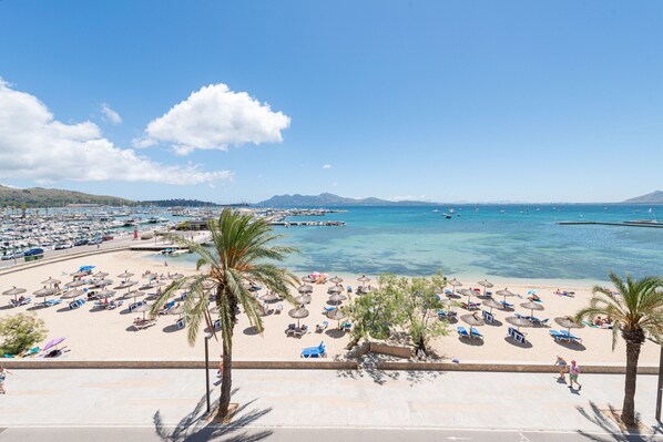 A beach with numerous umbrellas and sun loungers, a clear blue sky, and a calm sea. - Port de Pollença Esmeralda 3 (Port de Pollença)