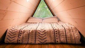 Una habitación con techo inclinado, paredes de madera, una cama con ropa de cama estampada y un ventanal.