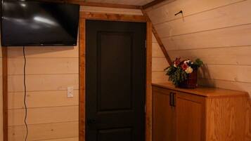 A room with a wooden ceiling, a black door, a TV mounted on the wall, and a bed with a fluffy blanket.