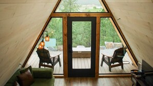 Habitación triangular con suelo de madera, sofá verde, televisor y vista al exterior a través de un gran ventanal.