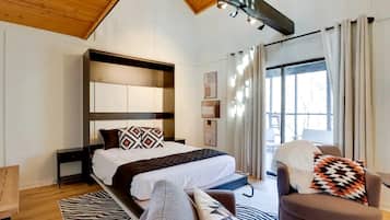 A modern bedroom with a bed, a chair, a sofa, a window, and a ceiling with exposed beams.