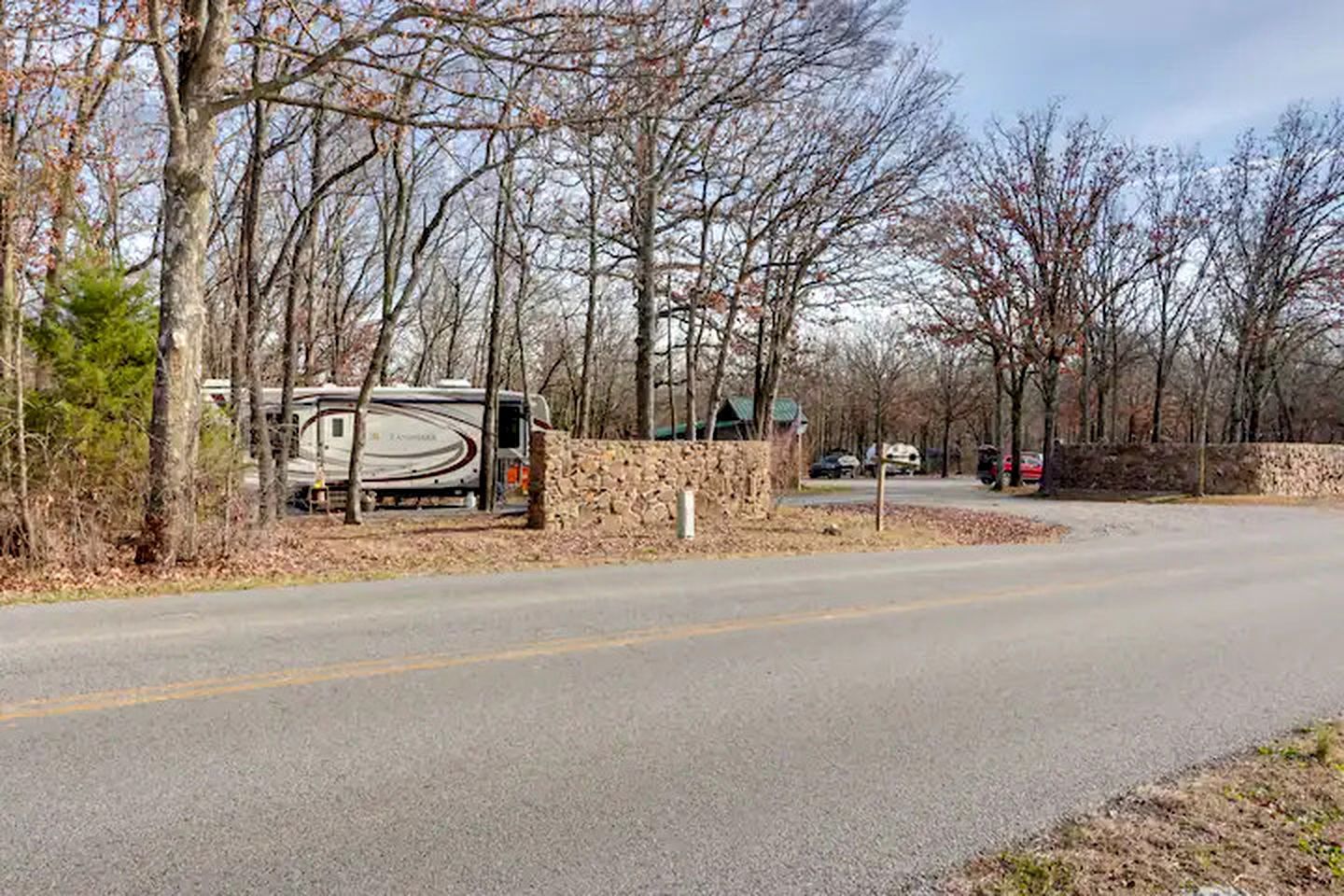 Une route bordée d’un muret en pierre et où est garé un camping-car.
