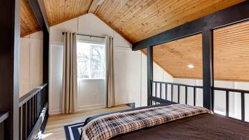 Un dormitorio con techo inclinado, una cama, un ventanal con cortinas y vistas al exterior.