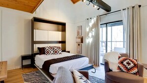 A modern bedroom with a bed, a chair, a sofa, a window, and a ceiling with exposed beams. - Secluded Studio Getaway with Outdoor Living and Trails Near Siloam Springs, Gentry, AR (Gentry)