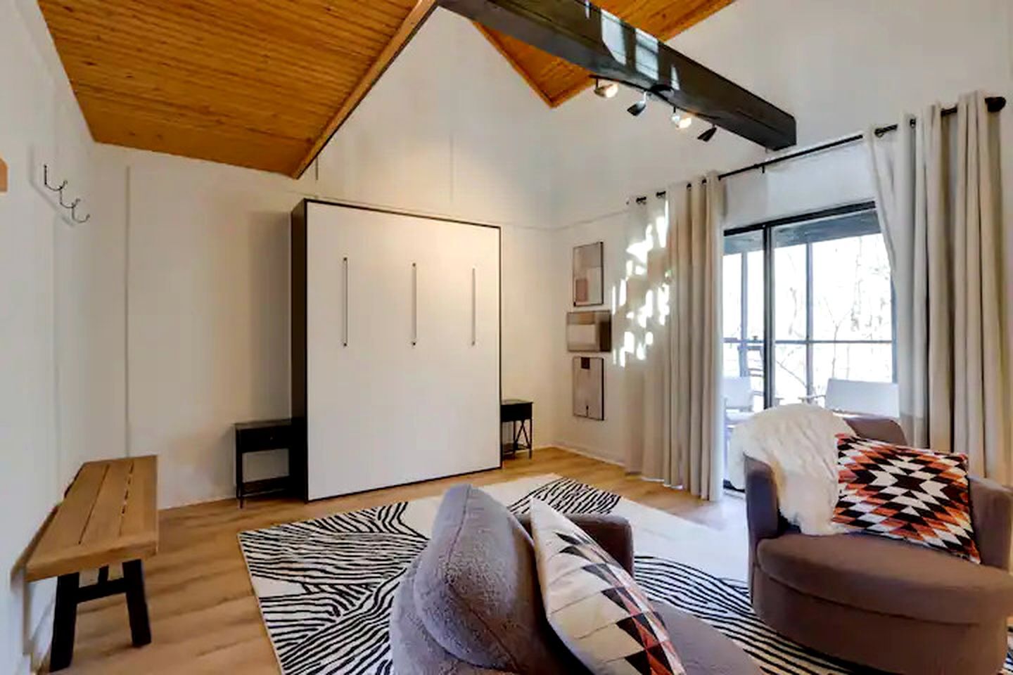 Een moderne woonkamer met een hoge plafond, een grote kast, een bank, een getextureerd vloerkleed en een raam met gordijnen.