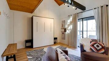 Een moderne woonkamer met een hoge plafond, een grote kast, een bank, een getextureerd vloerkleed en een raam met gordijnen.