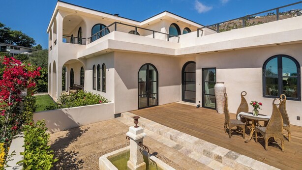 Una casa moderna de dos pisos con patio, mobiliario exterior y una fuente de agua.