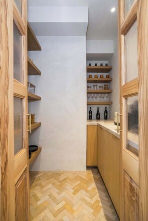 A narrow kitchen with wooden cabinets and shelves containing glassware and bottles.