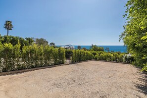 Un espace recouvert de gravier, offrant une vue sur la mer, entouré de verdure et agrémenté d’un portail en métal.